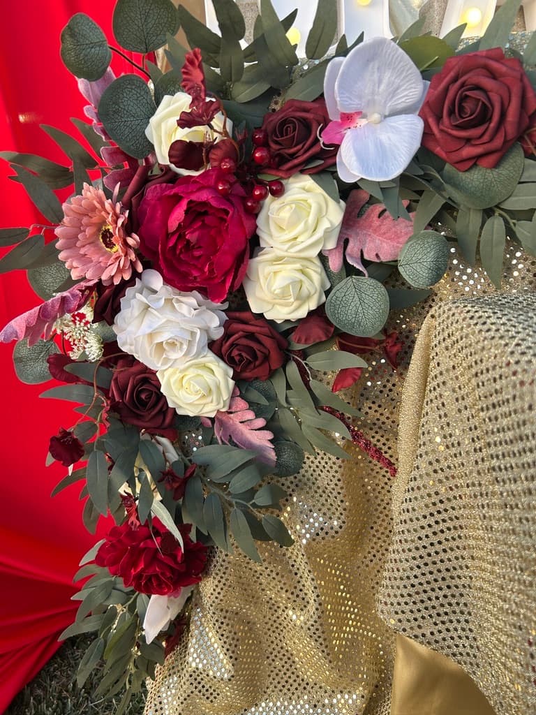 Arreglo floral de rosas color vino y marfil, una orquídea blanca y eucalipto sobre tela dorada de lentejuelas