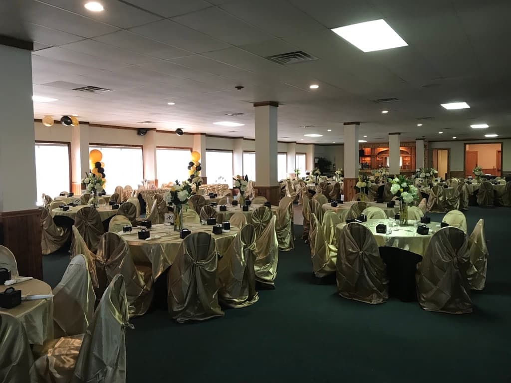 Salón de recepción preparado para una quinceañera, con fundas de silla de satín dorado, centros de mesa con flores blancas y globos negros y dorados