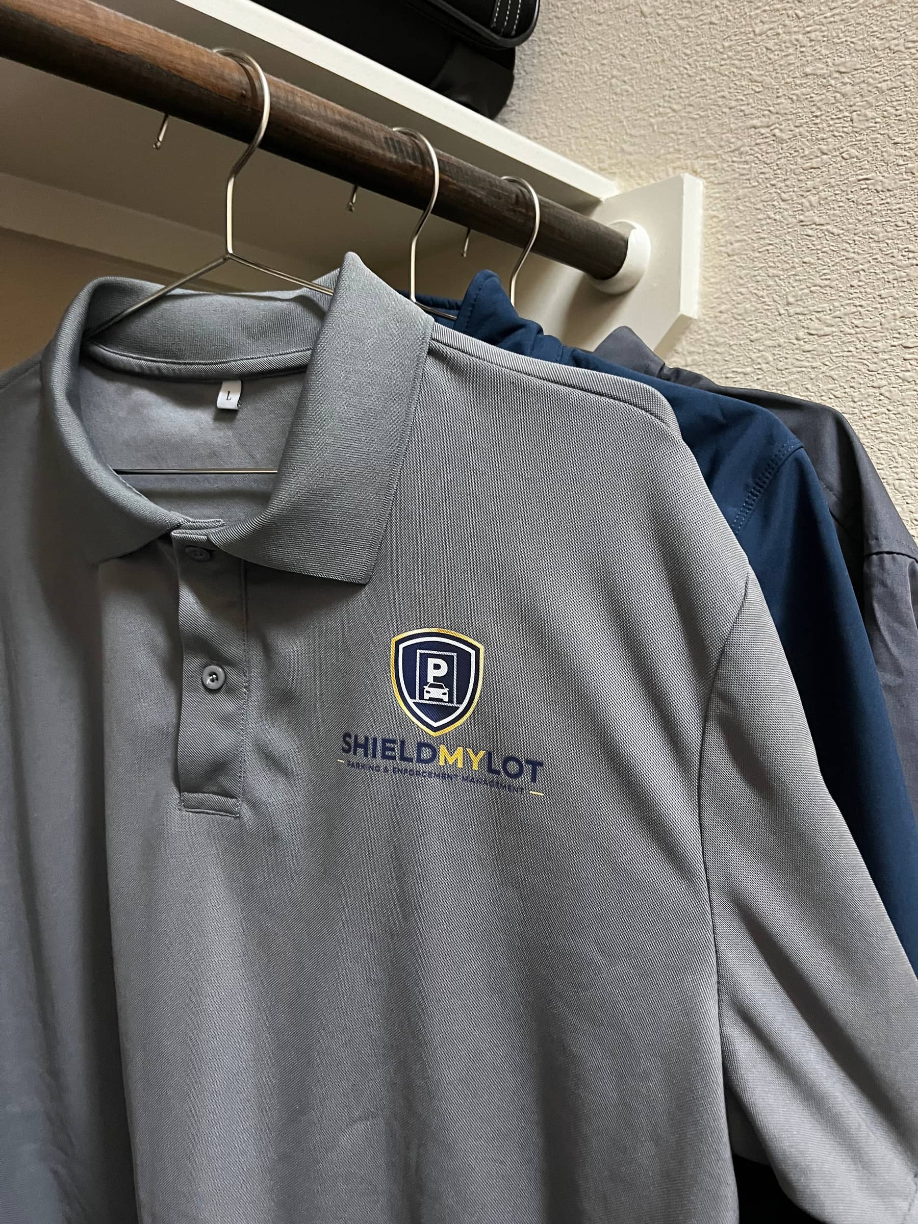 Playera polo gris en un gancho con el logo de ShieldMyLot impreso en el pecho, parte de la ropa personalizada que S&A hizo para el equipo de ShieldMyLot